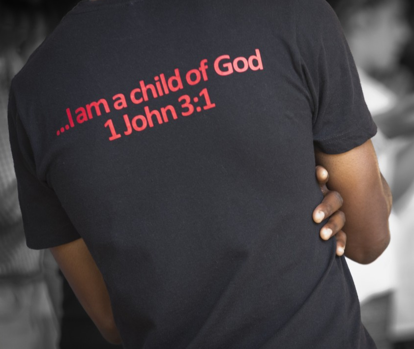a black person wearing a T-shirt with Bible verse "I am a child of God"