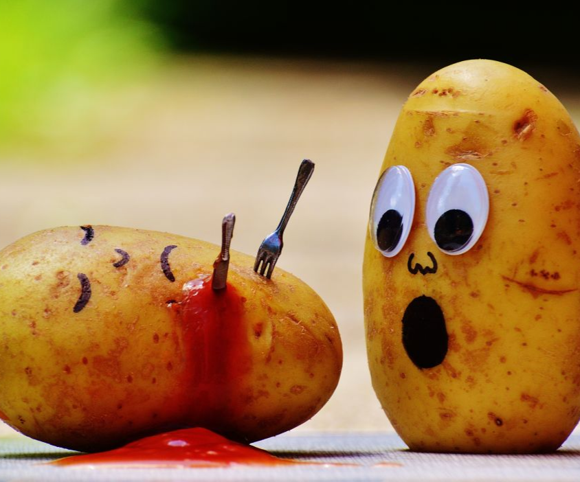 a potato stabbed with a knife and fork, bleeding ketchup